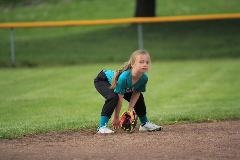 A young Winchester Little League softball player crouched in the infield, glove down, waiting for the pitch.