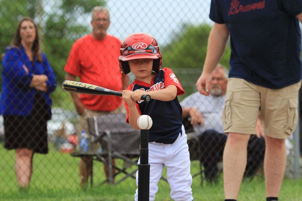 A young Winchester Little League player hitting off a batting tee while coaches and family look on.