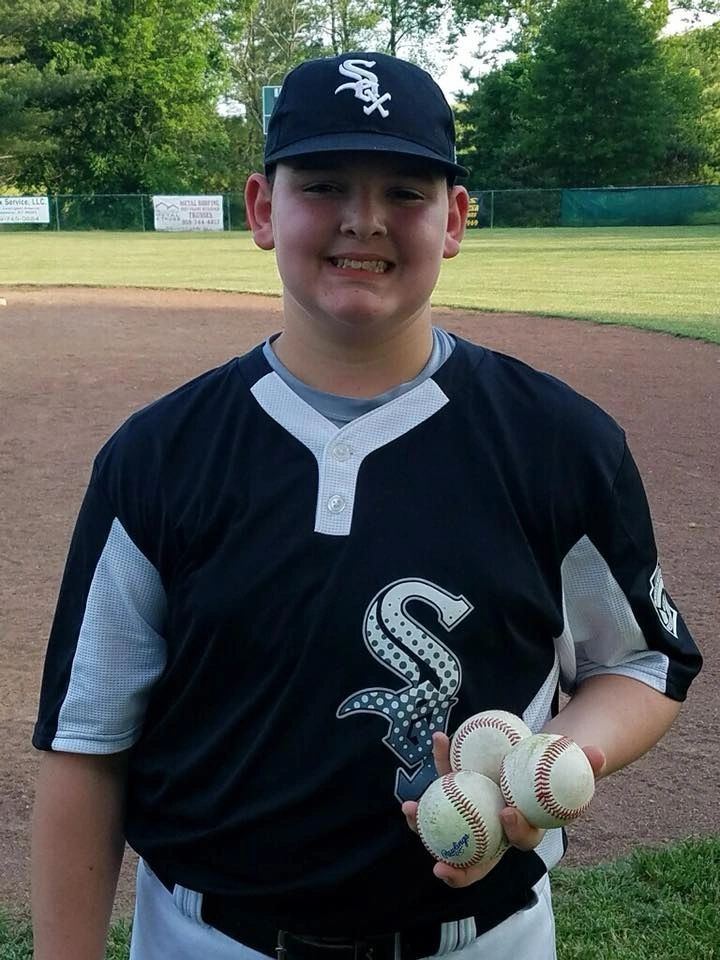 An older Winchester Little League baseball player in uniform holding game balls on the field.