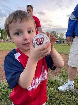 A young player holding up a baseball after a 2023 game.
